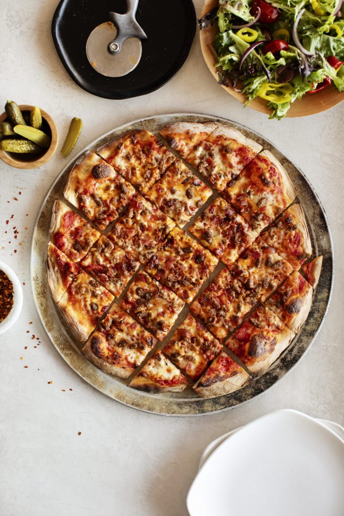 Beef and Bacon Cheeseburger Pizza party-cut on a pizza tray