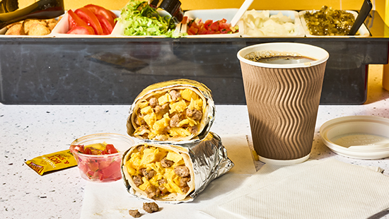 To-Go breakfast burrito cut in half next to a to-go cup of coffee on a convenience store counter.