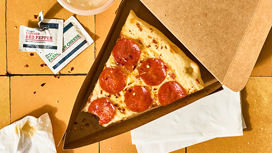 Slice of Pepperoni PIzza with a bite taken out of it in a convenience store triangle box.
