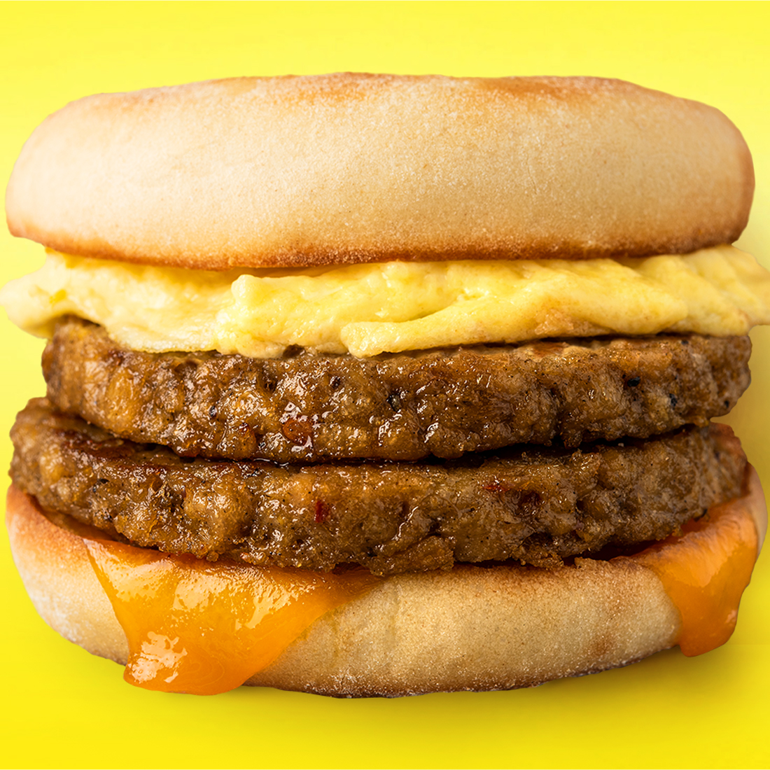 Close up of a breakfast sausage with egg, cheese, and plant-based sausage on a yellow gradient background