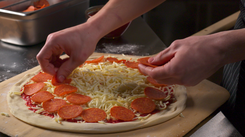 Chef placing pepperoni slices onto a pizza