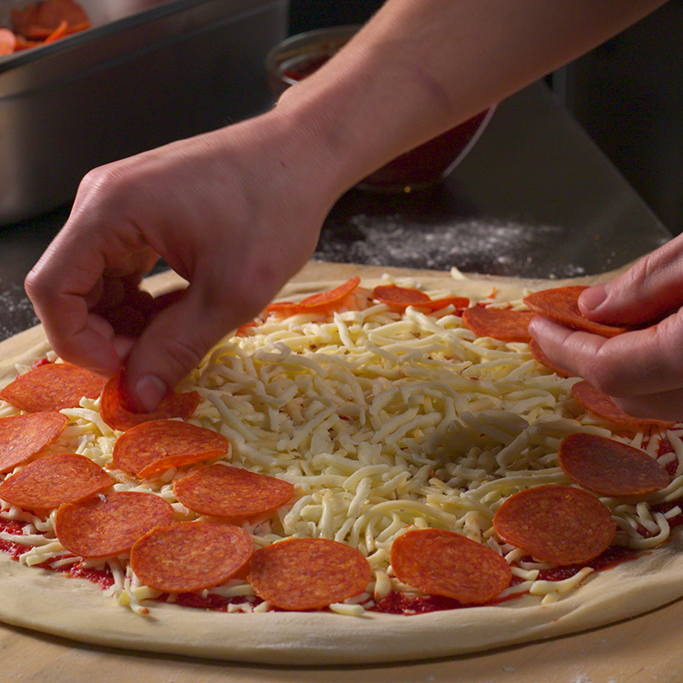 Chef placing pepperoni slices on a pizza