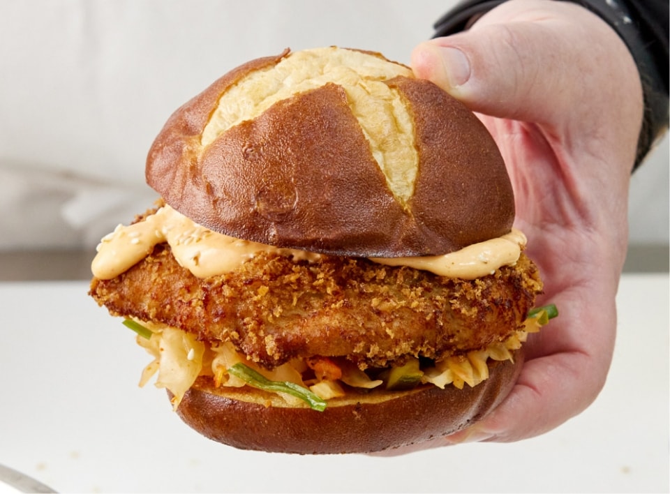 a hand holding a chicken sandwich on a pretzel bun