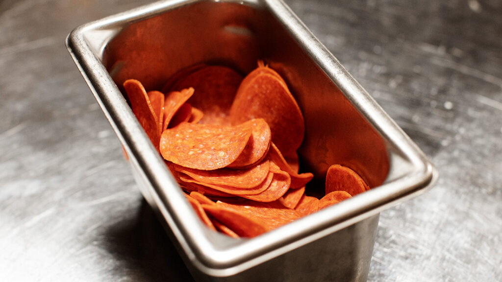 Container of pepperoni slices on a stainless steel countertop
