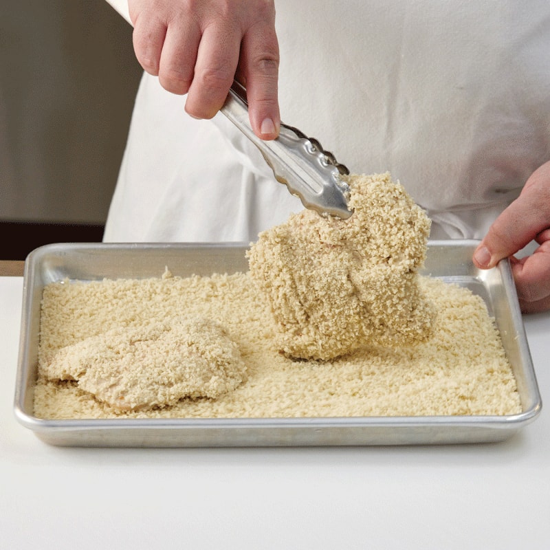 a chef applying panko crumbs to a chicken breast