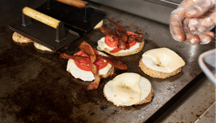 Bagel sandwiches on the griddle topped with egg, tomato, cheese and bacon