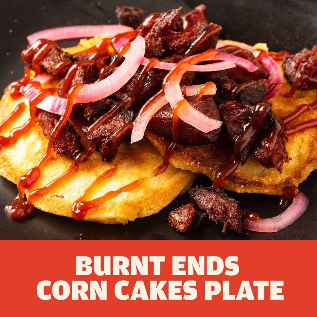 Burnt ends on top of yellow corn cakes topped with picked red onions and red sauce on a black plate