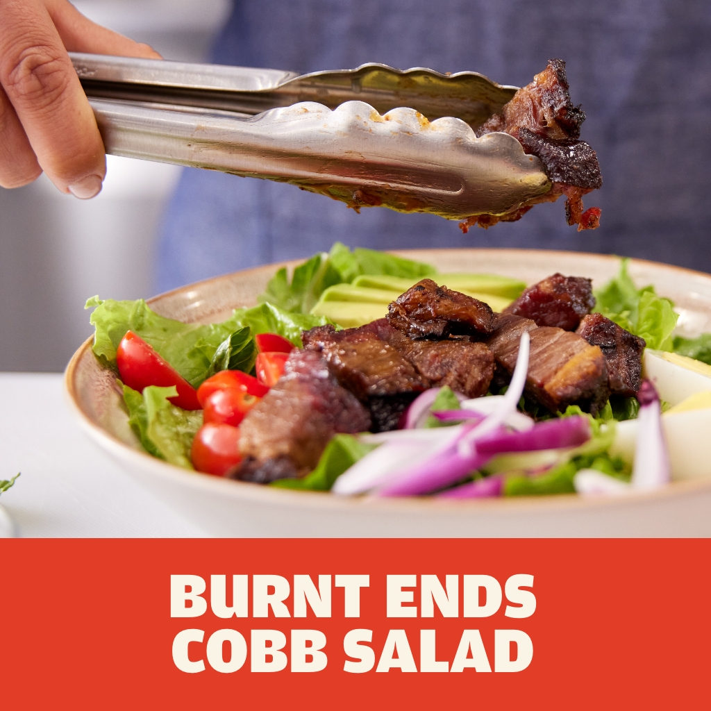 Austin Blues Burnt Ends on top of a cobb salad with bright green lettuce, grape tomatoes, red onions, halved hard boiled eggs and sliced avocado