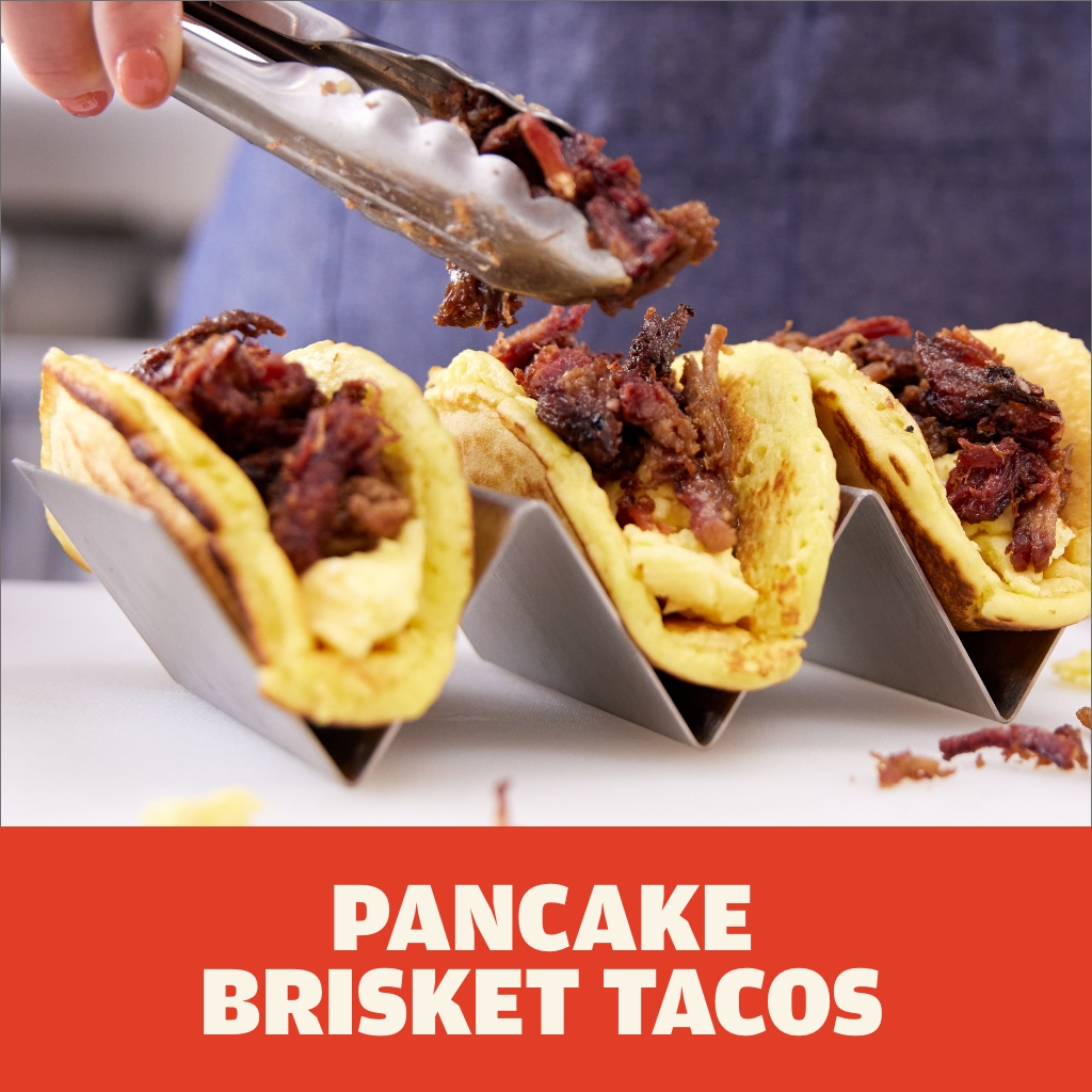 Austin Blues Pulled Brisket with scrambled eggs served inside tacos made with pancakes being prepared inside a stainless steel taco holder.