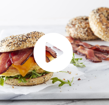 Two Breakfast bagel sandwiches made with Hormel Bacon 1 with a video play button overlay (click through to see video)