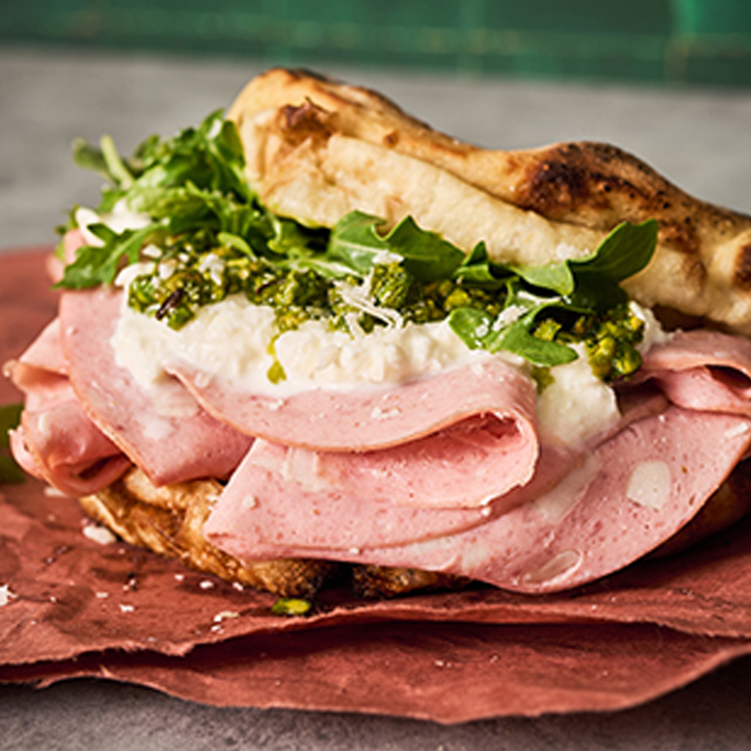 Columbus Mortadella Panuozzo with greens and burrata on red deli paper