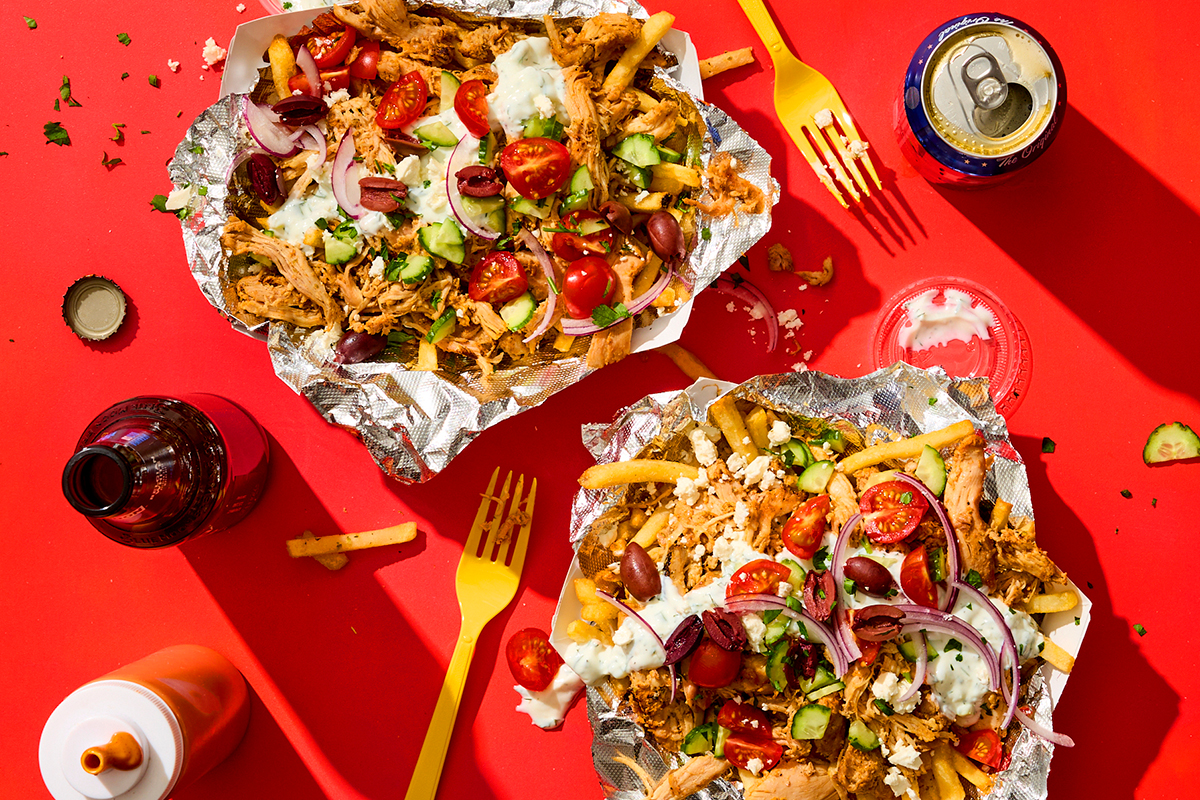 Trays of loaded dirty fries with drinks and garnishes on a red tabletop.