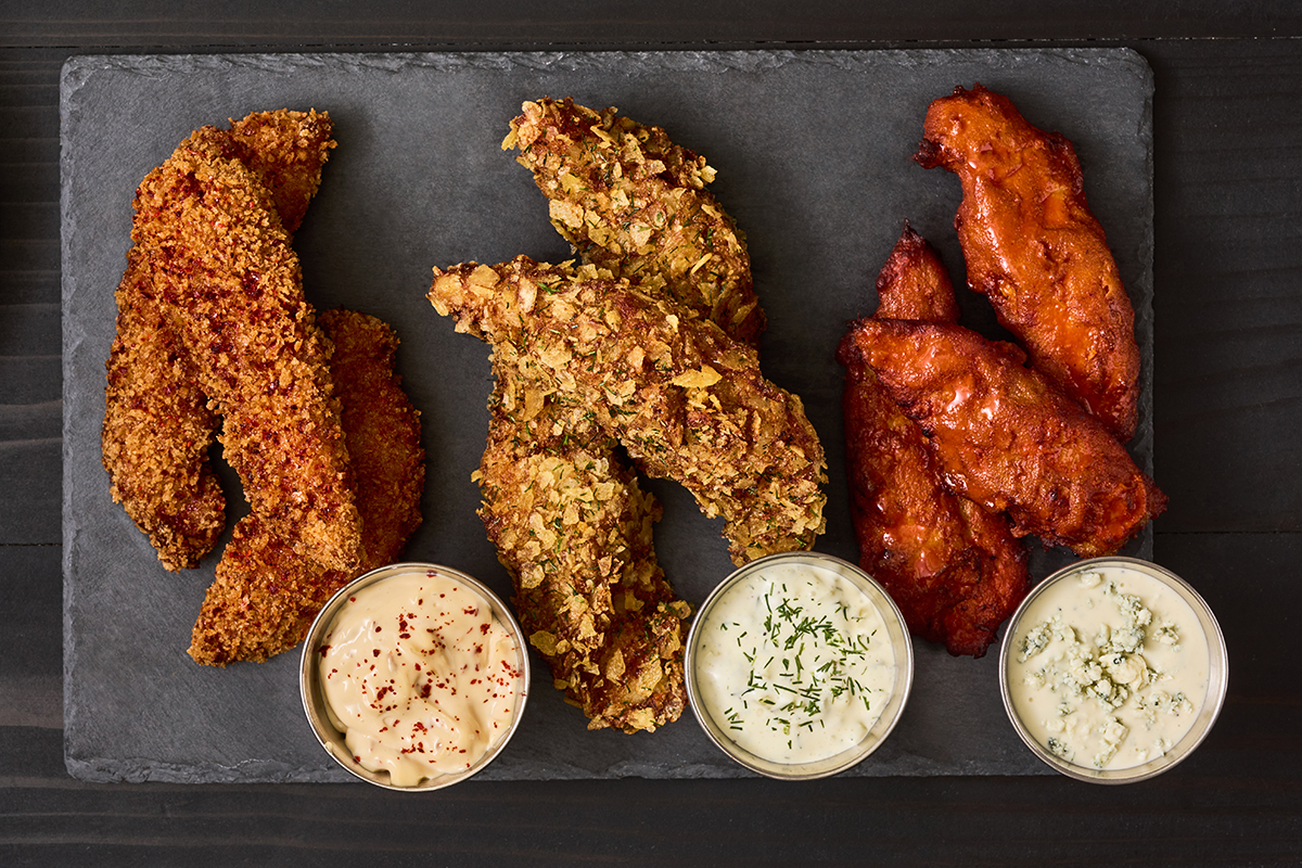 A trio platter of chicken tenders in different flavors with different sauces