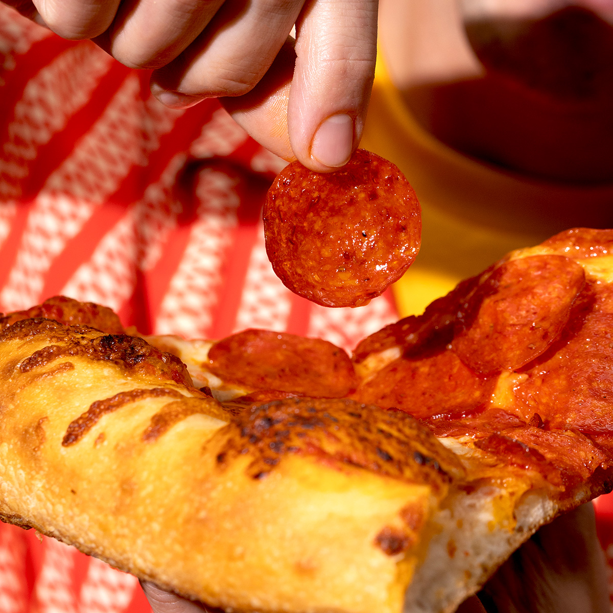 Person pulling a piece of HORMEL® THE PERFORMANCE PEPPERONI® Hot Calabrian Chili Pepperoni off of a slice of pizza