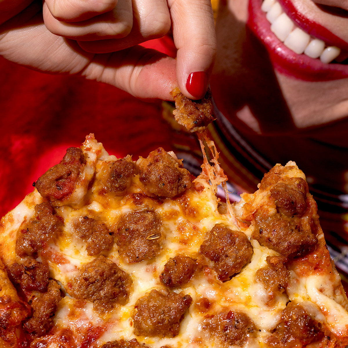 Person pulling a piece of FONTANINI® Hot Calabrian Chili Sausage Crumble off of a slice of pizza