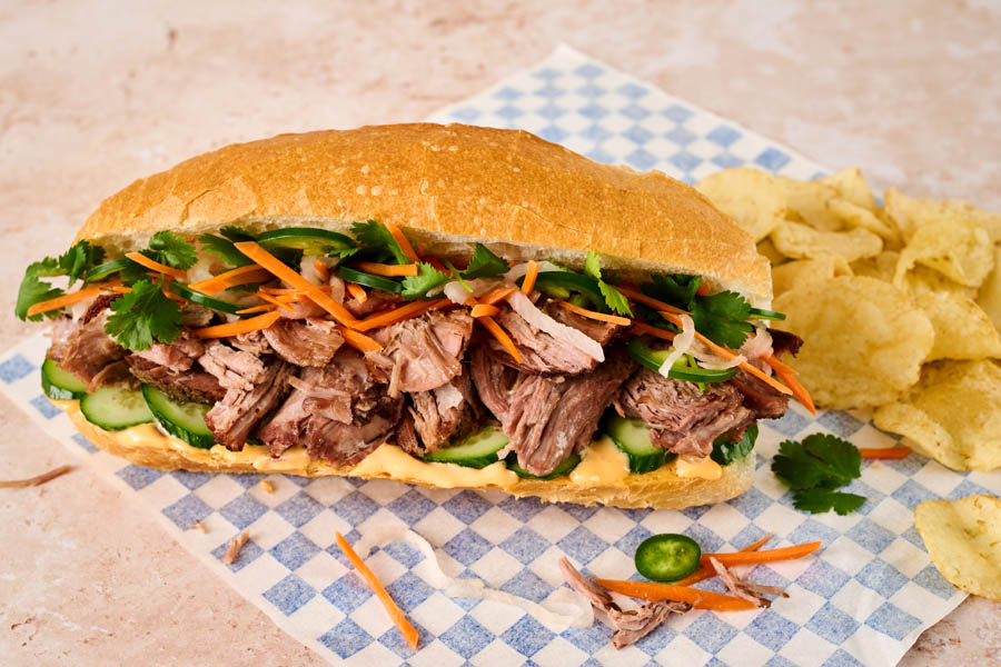 Pot roast banh mi sandwich on wax paper with a side of chips