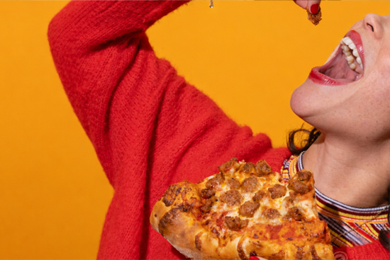 Woman holding pizza slice in one hand while preparing to take a bite of another piece of pizza sausage.