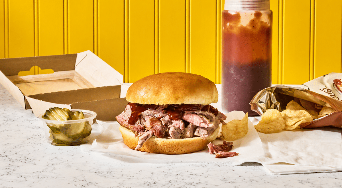BBQ pulled pork sandwich on a bun with pickles and potato chips